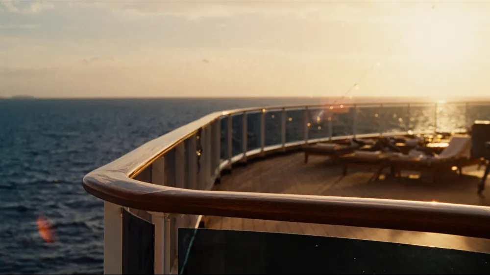 The sun deck of the Kruiseship at golden hour, loungers by the rail and the sea beyond